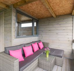 A covered porch with a wicker sectional sofa with pink cushions and a small glass table with flowers at Thornhills Lodge in Othery near Middlezoy