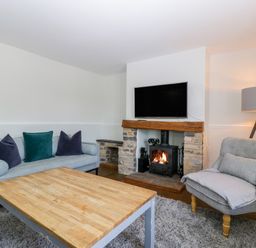 A living room with a gray sofa and armchair a wooden coffee table a fireplace with a TV above and a floor lamp at Somerset House in Othery near Middlezoy