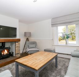 A living room with a wooden coffee table a gray armchair a sofa a fireplace with a fire and a TV mounted above it at Somerset House in Othery near Middlezoy