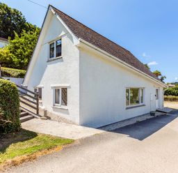 Exterior view of a white house with multiple windows and a sloping roof surrounded by bushes and trees at Baywatch Sands in Polzeath