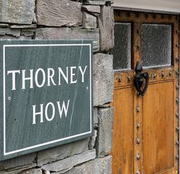 A stone wall with a green sign reading Thorney How next to a wooden door with glass panels