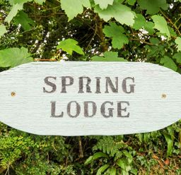 A wooden sign with the text Spring Lodge surrounded by green leaves and foliage at Eastcott near Kilkhampton