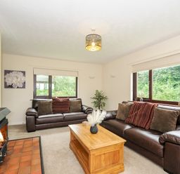 A living room with two brown leather sofas a wooden coffee table a fireplace and large windows at Spring Lodge in Eastcott near Kilkhampton