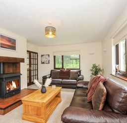 A living room with two brown leather sofas a wooden coffee table a fireplace and windows showing greenery at Spring Lodge in Eastcott near Kilkhampton