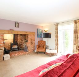 A living room with a brick fireplace a red sofa an armchair a wall-mounted television and curtains at Willow Cottage in Hickling near Catfield