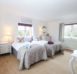 A bedroom with two single beds side by side white furniture and windows with curtains at Willow Cottage in Hickling near Catfield