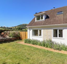 A garden with a lawn wooden chairs and a white house with windows at Cam O'r Fechan Annexe in Llangollen