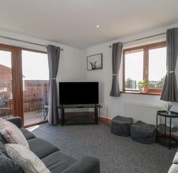 A living room with a sofa television two poufs a side table and large windows with curtains at Bluebell Lodge Meadow view lodges in Brean