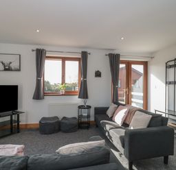 A living room with two grey sofas two poufs a TV on a stand a window and a door with glass panels at Bluebell Lodge Meadow view lodges in Brean