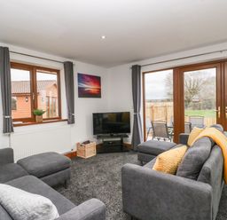A living room with two gray sofas cushions a television and large windows at Delphine Lodge Meadow View Lodges Brean