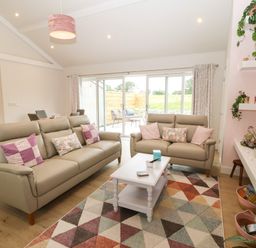 A living room with two sofas a coffee table and sliding glass doors at Y Beudy in Dinas near Bontnewydd