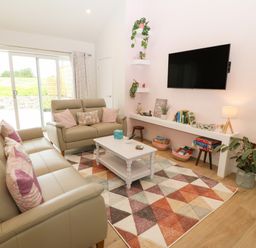 A living room with beige sofas a white coffee table a colorful triangular patterned rug and a wall mounted TV at Y Beudy in Dinas near Bontnewydd