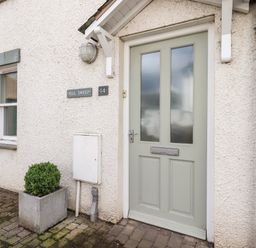 An exterior view of a front door with frosted glass panels a window and a potted plant at Fell Sweep in Keswick