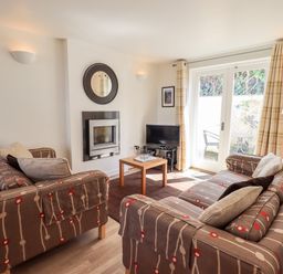 A living room with two patterned sofas a small wooden coffee table a fireplace and glass doors leading outside at Fell Sweep in Keswick