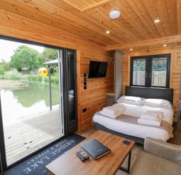 A bedroom with a bed and a television at Maple Lodge at Bridge Lake Farm & Fishery Chacombe