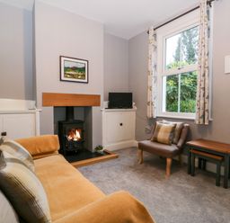 A living room with a sofa a fireplace a small chair and nested tables at 7 Railway Cottages in Newby Bridge