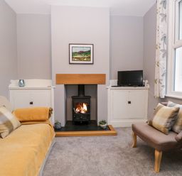 A living room with a fireplace between two white cabinets one holding a television and two sofas with cushions at 7 Railway Cottages in Newby Bridge