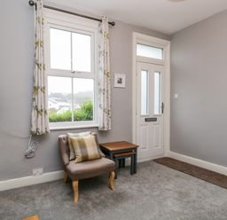 A corner of a room with a window and white door a beige armchair with cushions and two nested tables at 7 Railway Cottages in Newby Bridge
