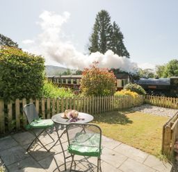 A small garden with patio furniture and a steam train passing behind a wooden fence at 7 Railway Cottages in Newby Bridge