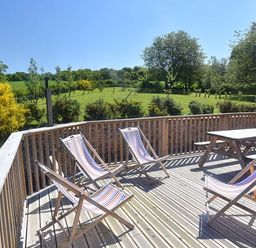 A wooden deck with four striped deckchairs and a wooden picnic table overlooking a grassy field with trees at Skylarks in Ferintosh near to Dingwall