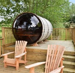 A wooden deck with two wooden chairs and a barrel-shaped pod surrounded by trees at Skylarks in Ferintosh near to Dingwall