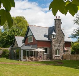 A stone house with a slate roof and a patio table with an umbrella in a garden at Beltie Lodge in Borgue