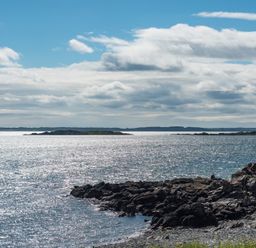 A rocky shoreline with water and small islands under a partly cloudy sky at Beltie Lodge in Borgue
