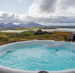 An outdoor hot tub with bubbling water overlooking a grassy landscape with hills and a body of water at Eagle Lodge in Uig near Stornoway