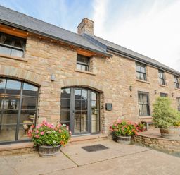 A stone exterior of a building with arched windows, doors, and flower pots at Pen Bont Home Farm in Upper Chapel near Builth Wells