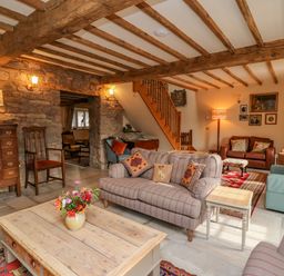 A living room with sofas a wooden coffee table flowers on the table and exposed wooden beams at Pen Bont Home Farm in Upper Chapel near Builth Wells