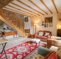 A living room with wooden stairs a red patterned rug and leather sofas at Pen Bont Home Farm Upper Chapel near Builth Wells