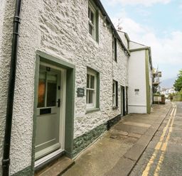 A stone exterior cottage with a green door and windows along a narrow street at Style Cottage in Keswick