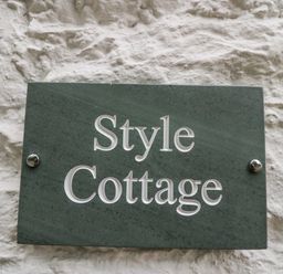 A green plaque with Style Cottage text on a white textured wall at Style Cottage in Keswick
