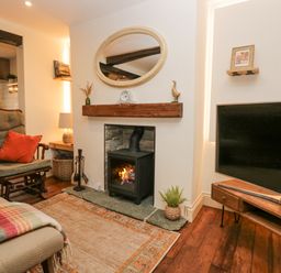 A living room with a fireplace rocking chair rug and television at Style Cottage in Keswick