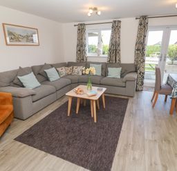A living room with a gray sectional sofa brown armchair coffee table and dining table at Atlantic Reach in Marazion
