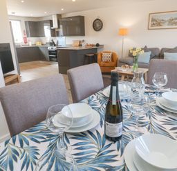 A dining table with set plates and glasses and a bottle in an open kitchen and living area at Atlantic Reach in Marazion