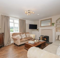 A living room with beige sofas a wooden coffee table a fireplace and a TV on the wall at Skylarks in No Mans Land near Looe