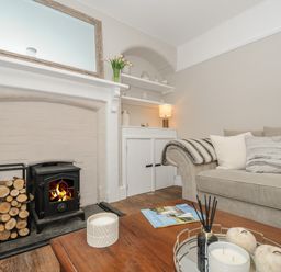A living room with a fireplace logs throw on a couch and candles on a wooden table at Skylarks in No Man's Land near Looe