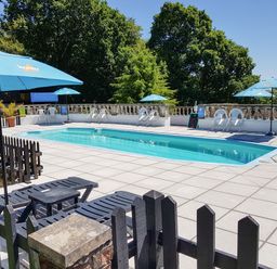 An outdoor swimming pool with white plastic chairs and blue umbrellas surrounded by trees at No 51 Valley Lodges Honicombe Manor near Gunnislake