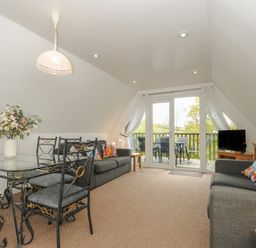 A living room with a glass dining table and chairs two grey sofas with colorful cushions and glass doors leading to a balcony at No 51 Valley Lodges Honicombe Manor near Gunnislake