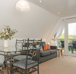 A dining area with glass table and metal chairs next to a sofa with colorful cushions and a balcony door at No 51 Valley Lodges Honicombe Manor near Gunnislake