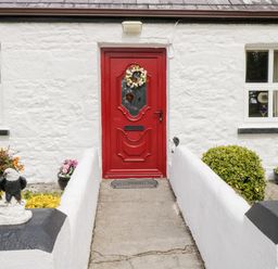 Front entrance with a red door flanked by white walls and eagle statues at Cartron Cottage Ballintubber County Mayo