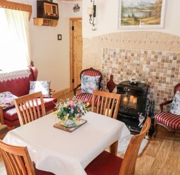 A dining area with wooden table and chairs a red loveseat two armchairs with striped upholstery a stove and tiled wall at Cartron Cottage Ballintubber County Mayo