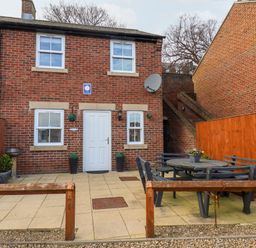 A brick house with white door and windows a patio with outdoor table and benches and wooden fences at Stoker's Rest in Whitby