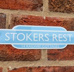A blue sign with white text reading Stokers Rest 14 Railway Cottages on a brick wall at Stokers Rest in Whitby
