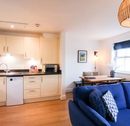 A kitchen area with white cabinets and black countertop next to a dining table and blue sofa at Stoker's Rest Whitby