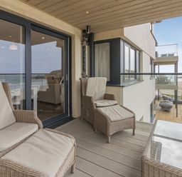 A balcony with cushioned wicker chairs and a glass table overlooking the beach at Apartment 18 Burgh Island Causeway Bigbury-On-Sea