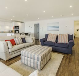 A living room with sofas and a striped ottoman next to a kitchen area at Apartment 18 Burgh Island Causeway in Bigbury-On-Sea