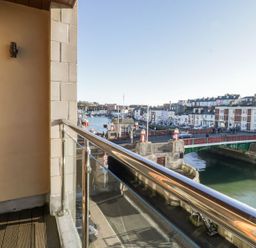 A balcony with glass and metal railing overlooking a river and a bridge with buildings along the riverbank at Townbridge Apartment in Weymouth