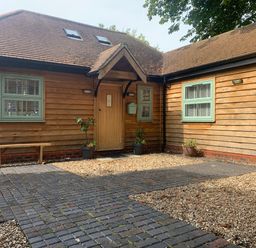 A wooden exterior of a house with a paved walkway and potted plants at Dreamwood Lodge in Keston near Leaves Green